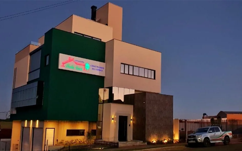 Prédio da sede da Loteadora Bella Casa em Borrazópolis-PR, ao anoitecer, com o letreiro iluminado